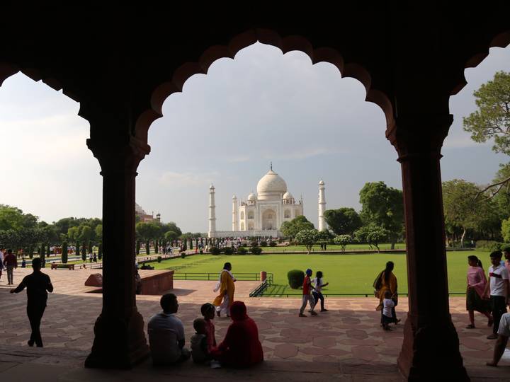 Iconic view of the Taj Mahal framed by an ornate arch with visitors strolling through the garden courtyard.