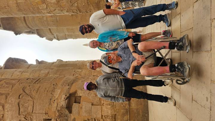 A diverse group poses between towering hieroglyph-covered columns with a distant obelisk visible.
