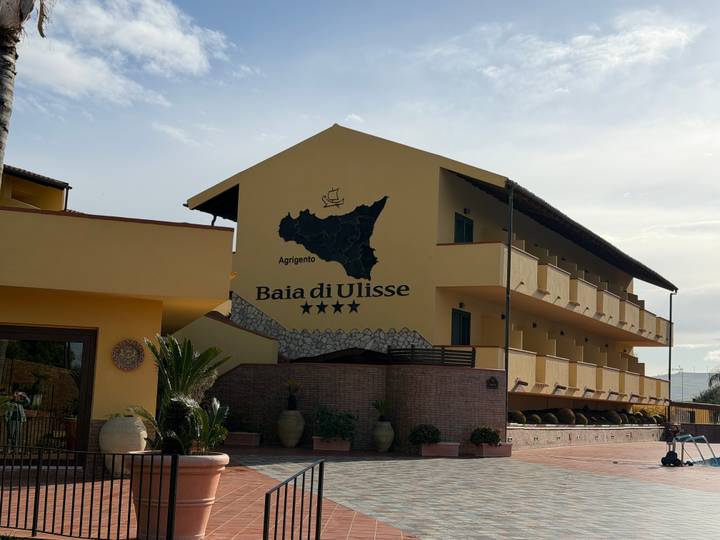Yellow hotel building with a map of Sicily and the text 'Baia di Ulisse' displayed on its facade.