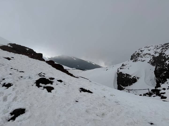Snow-covered volcanic slopes and dark lava rocks rise into misty clouds on a wintry mountainside.
