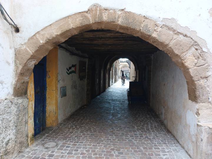 Dim stone tunnel passageway in old medina with a cyclist silhouette in distance