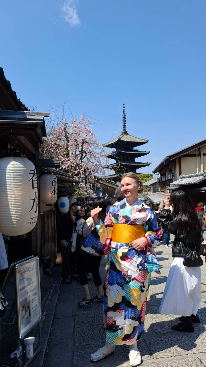 Woman in colorful kimono posing on a traditional street lined with cherry blossoms and a five-story pagoda.