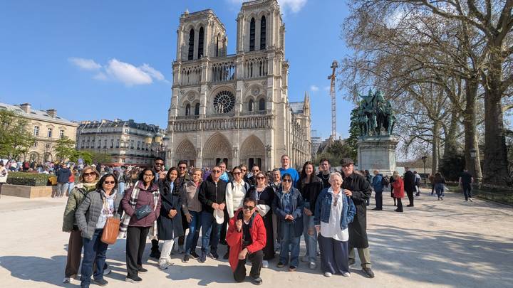 A tour group poses in front of the twin-tower façade of Notre-Dame Cathedral on a sunny day.
