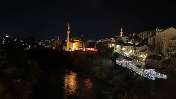 Nighttime riverside town with illuminated mosques and reflections shimmering on dark water.