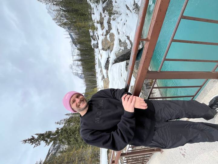 Traveller leaning on a bridge over turquoise river with snowy forest and peaks in Yoho.