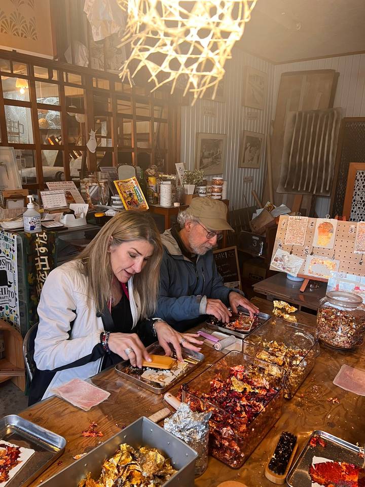 Travellers concentrate while crafting delicate items in a cozy Japanese workshop filled with materials.