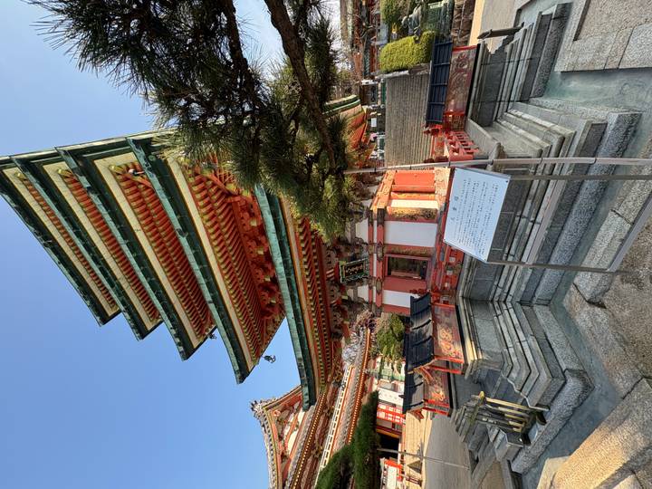 Multi-tiered pagoda with vivid green eaves and red beams rises sharply against a clear sky.