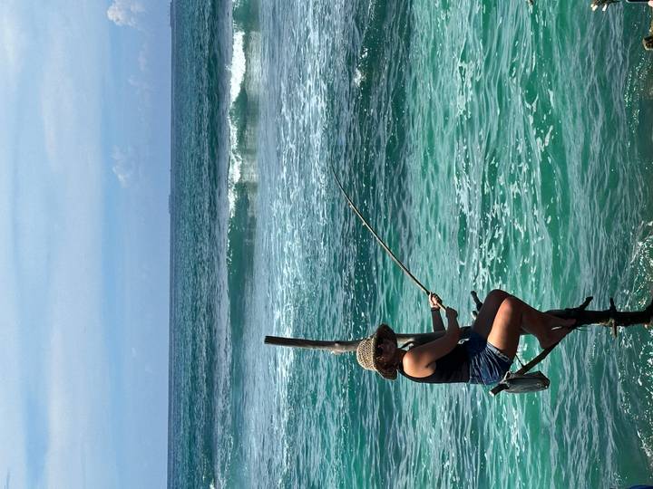 Woman perched on a stilts pole practices traditional fishing above turquoise ocean water.