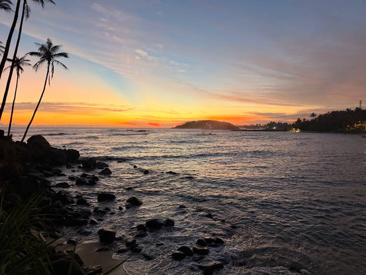 Vibrant twilight sky glows over a rocky coastline and distant headland in Sri Lanka.