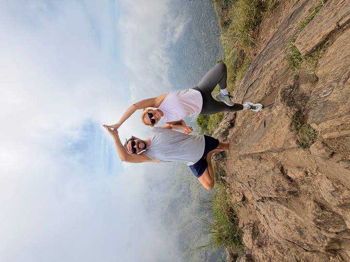 Fit couple strikes a playful yoga pose atop a misty mountain viewpoint.
