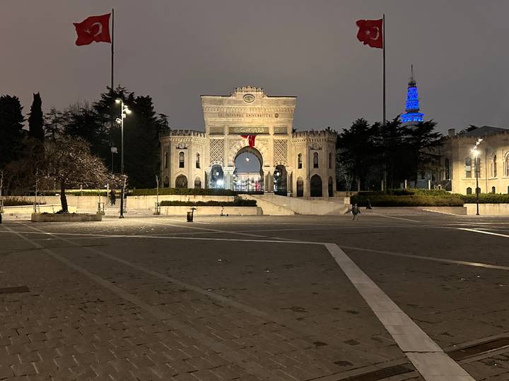 Evening view of Istanbul University’s historic gate illuminated against the night sky.