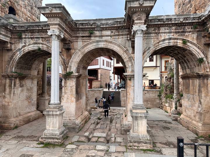 Ancient stone arches of Hadrian’s Gate in Antalya frame visitors walking through the old city entrance.