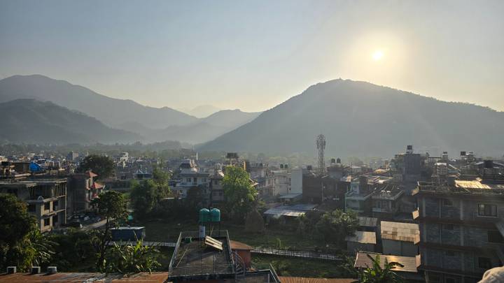 Morning sun over Pokhara’s rooftops and surrounding verdant hills with light mist.