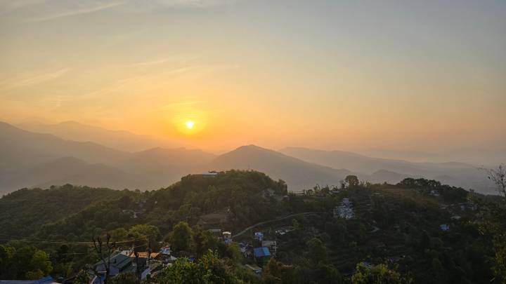 Soft orange sunrise lighting Himalayan foothills and small village houses below.