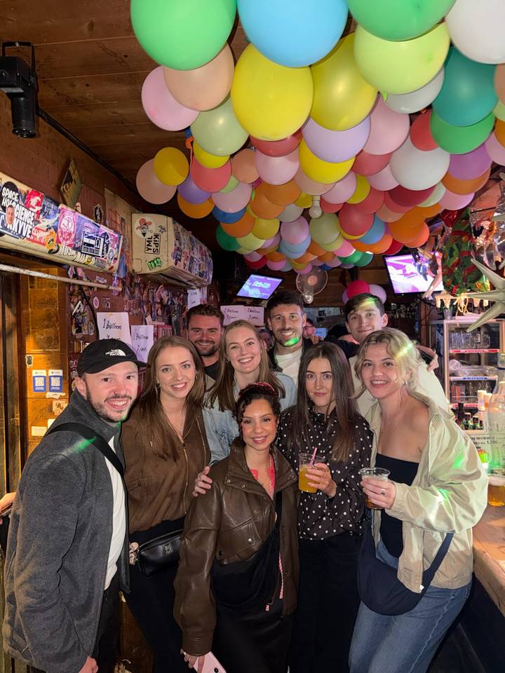 Friends gathered inside a lively bar decorated with colorful balloons.