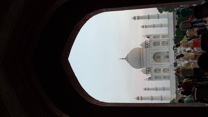 Taj Mahal framed by a dark arched gateway at dusk with visitors gathered in the foreground.