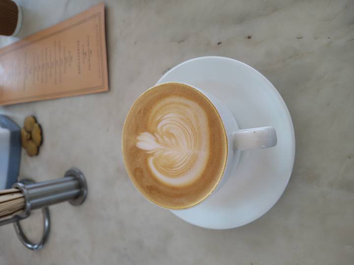 Latte with leaf art served in a white cup on a marble table beside a menu.