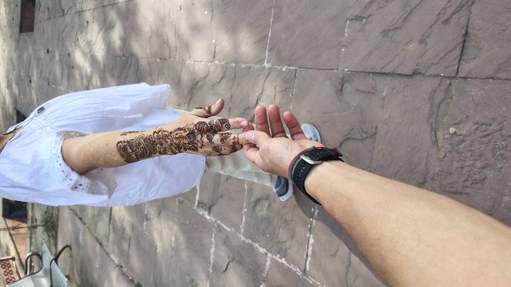 Close-up of two travelers holding hands, one with intricate henna designs, walking on a stone courtyard.