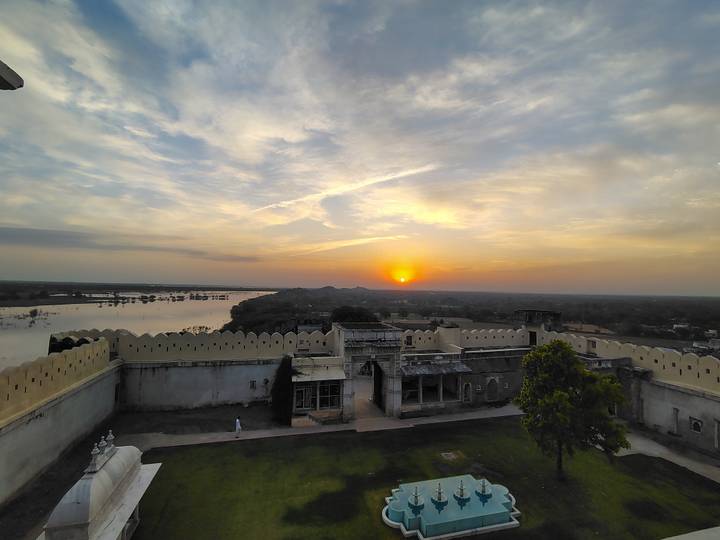 Scenic sunset over a riverside fort complex and distant hills.