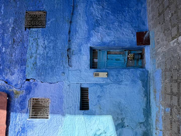 Weathered blue wall with a rustic wooden door and small flower pot in Chefchaouen.
