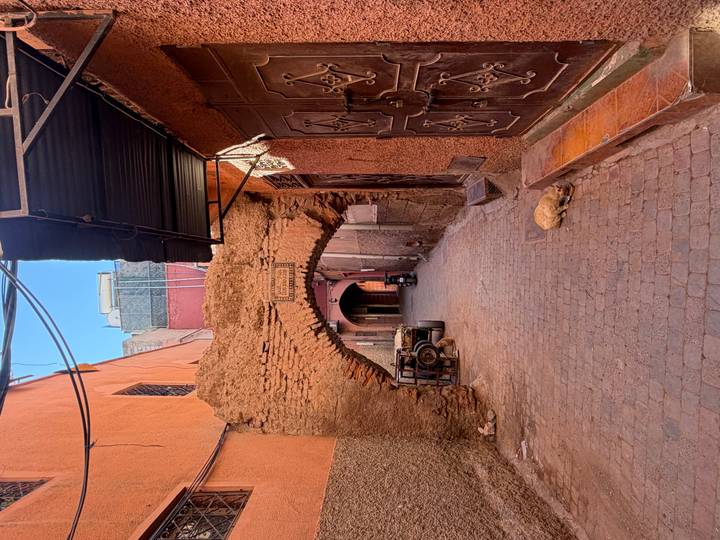 Narrow reddish alley in Marrakesh medina with crumbling arch and resting cat.