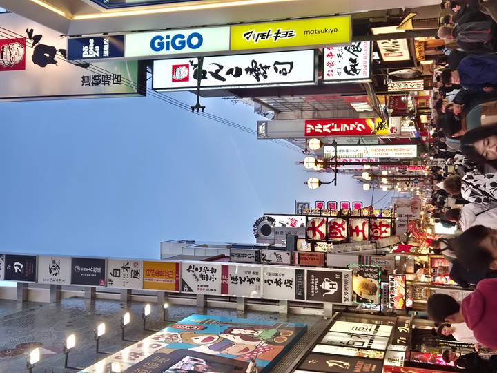 Bustling neon-lit shopping street filled with crowds and signboards in Osaka.