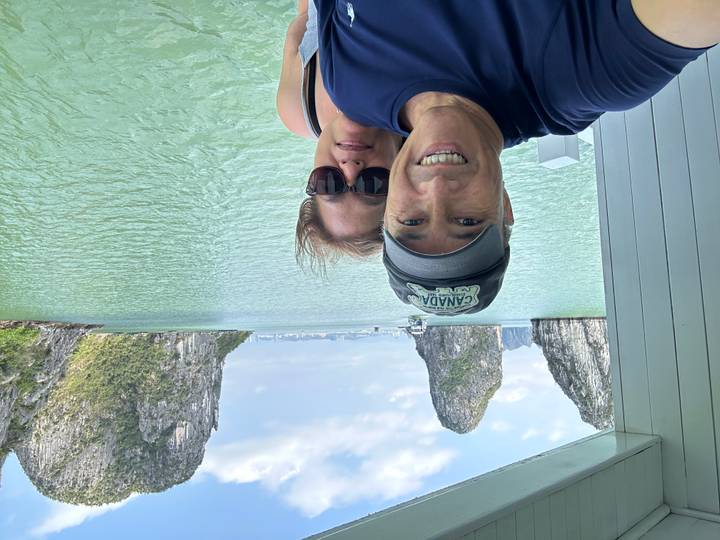Smiling couple taking a selfie on a boat with towering karst islands in the background.