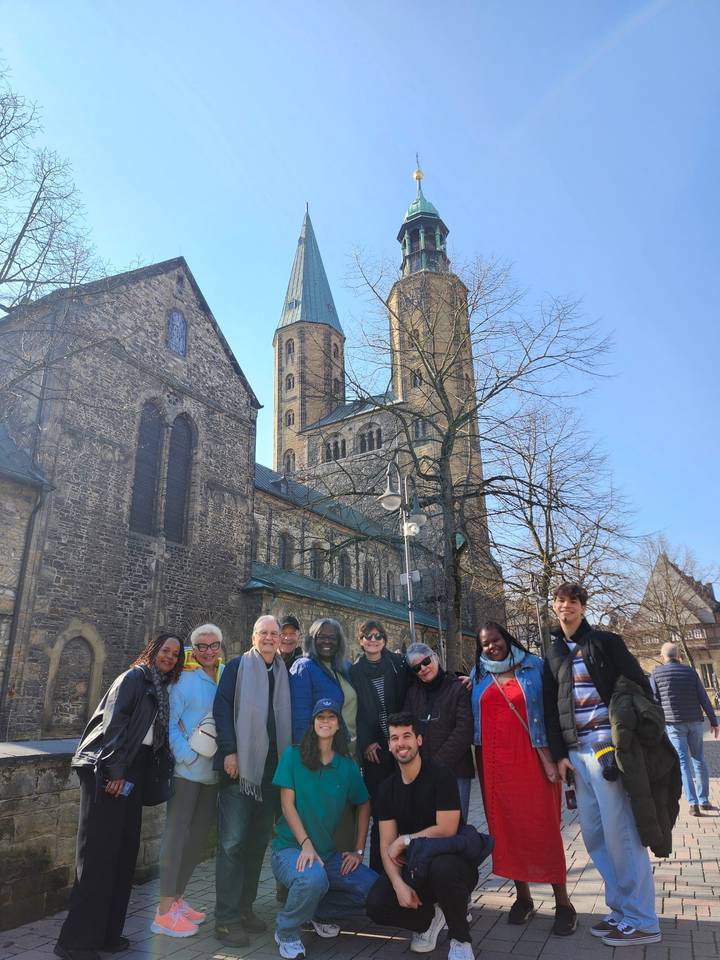 Smiling tour group posing outside a historic stone church on a sunny day.