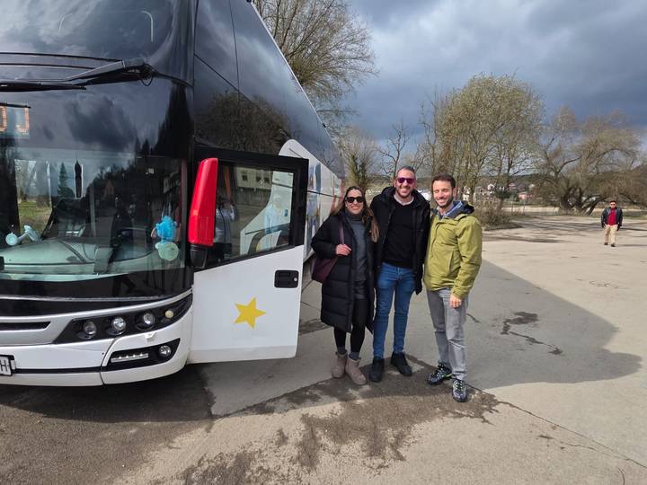 Tour passengers smiling beside a white coach bus with a star logo on a cloudy day.