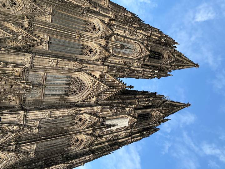 Dramatic upward perspective of the twin spires and ornate facade of Cologne Cathedral against a blue sky.