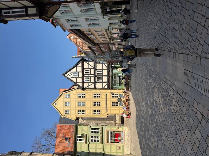 Charming cobblestone square lined with colourful half-timbered houses under a clear blue sky, with tourists strolling.