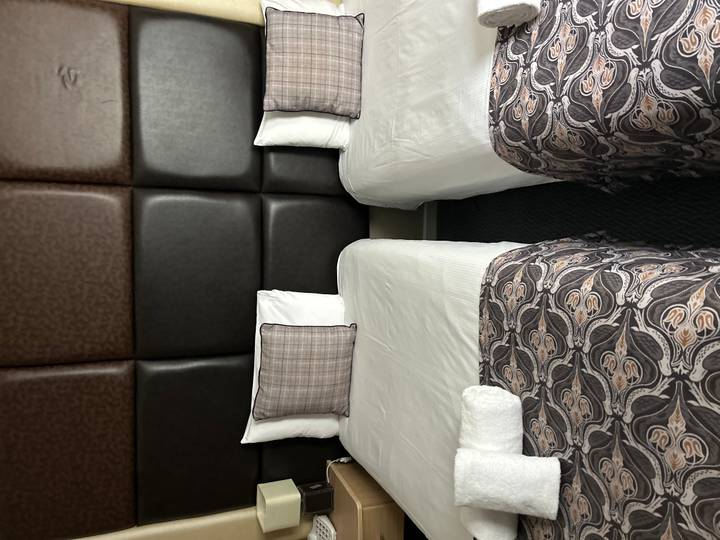 Simple twin hotel beds with patterned runners and plaid cushions in a compact room.