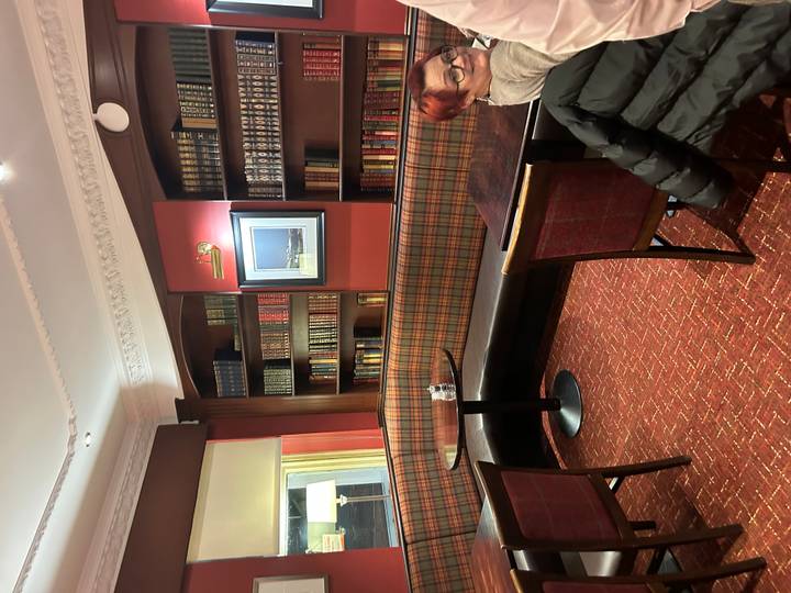 Cozy lounge with tartan upholstery, dark wood bookshelves, and small café tables in a traditional hotel.