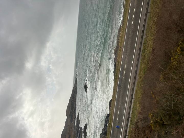 Moody coastal scene with crashing waves and a winding road along Scotland’s rocky shoreline.