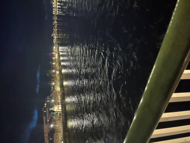 Nighttime riverside scene with city lights reflecting on dark, rippled water.