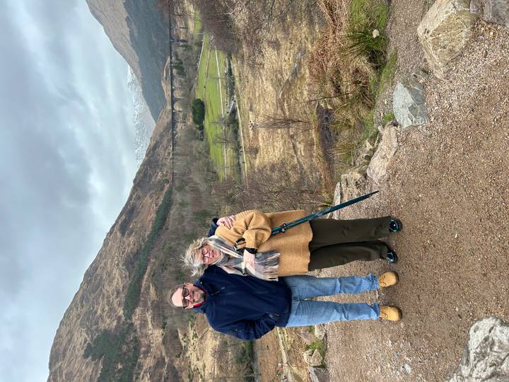 A couple poses at a viewpoint overlooking the iconic Glenfinnan Viaduct amid rugged Highlands scenery.