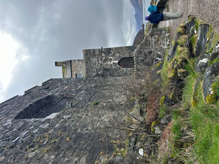 Close view of weathered stone walls and doorway of a historic Scottish castle beside mossy rocks.