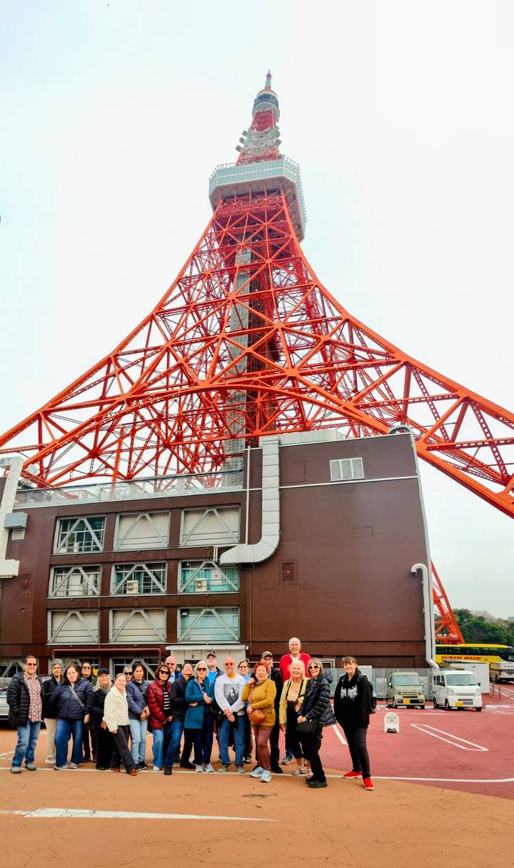 The vivid orange lattice of Tokyo Tower rises into a pale sky viewed from its base.