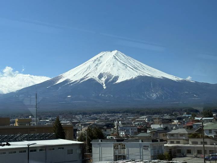 Snow-capped Mount Fuji dominates the horizon above a Japanese town under a clear blue sky.