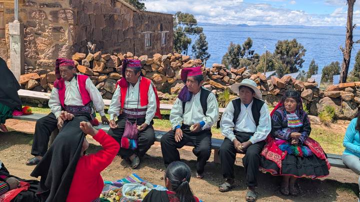 Traditional community gathering with Lake Titicaca visible behind men in embroidered waistcoats and women in bright skirts.
