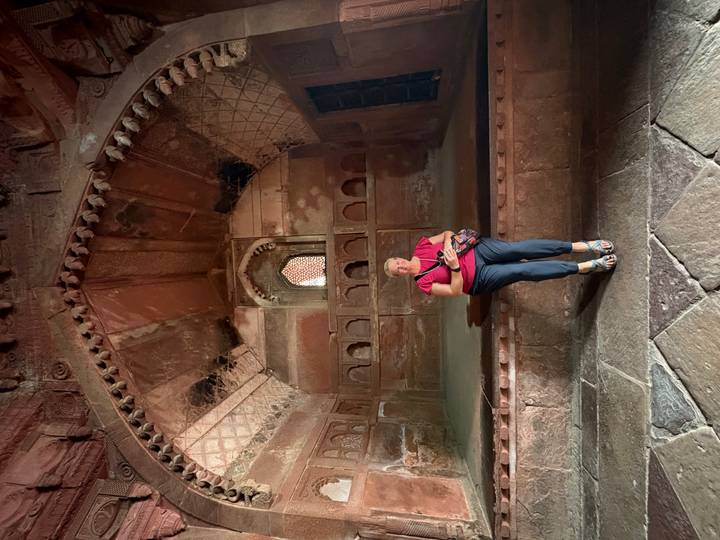 Traveller seated inside an ancient red-sandstone chamber with vaulted decorative ceiling and arched niches.