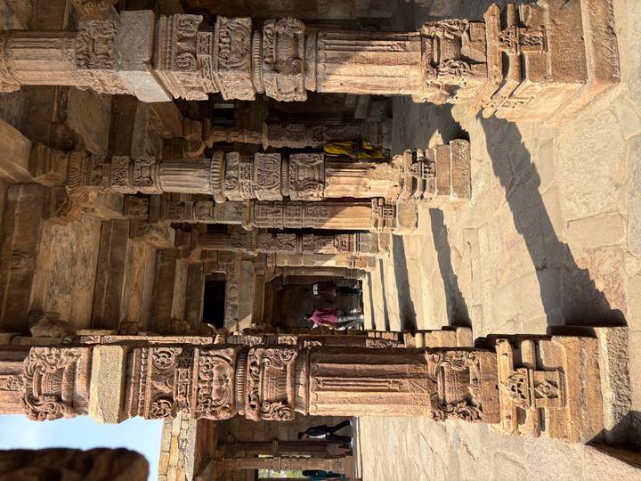 Stone pillars covered in ornate Hindu carvings illuminated by warm sunlight at an ancient temple.