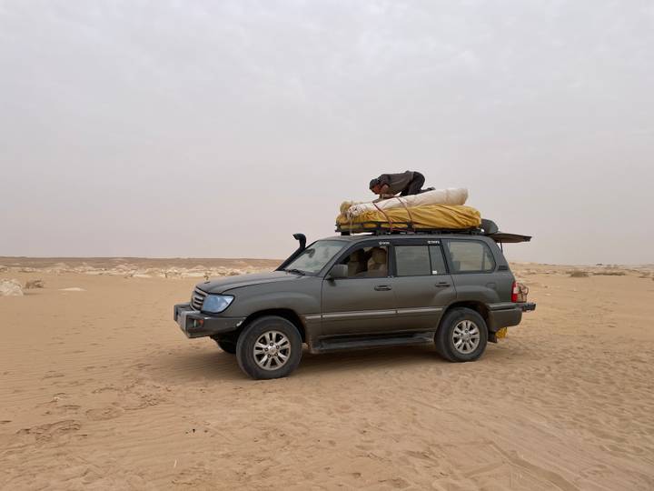 4x4 vehicle loaded with camping gear parked on vast sandy desert under hazy sky.