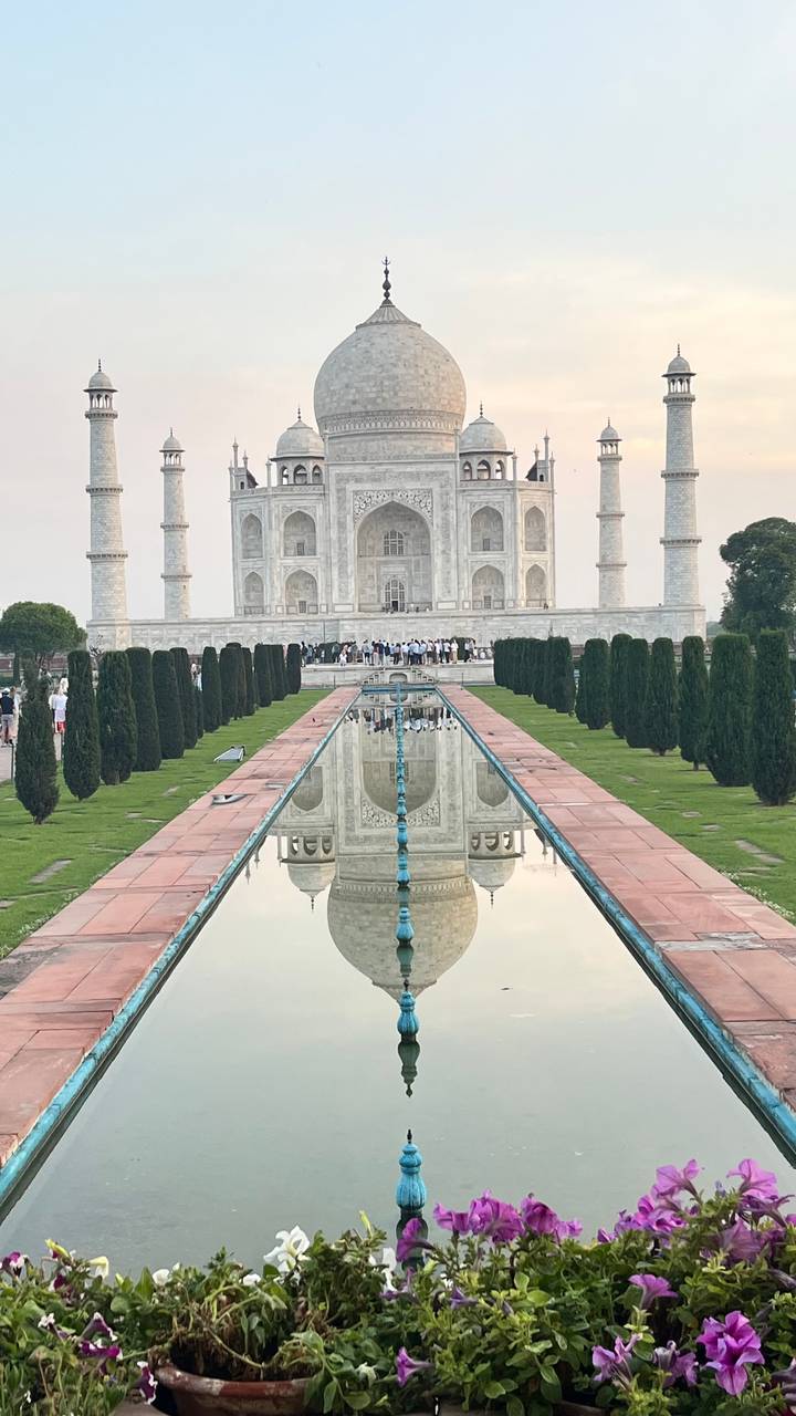 Symmetrical view of the Taj Mahal with its reflection in the long pool flanked by cypress trees.