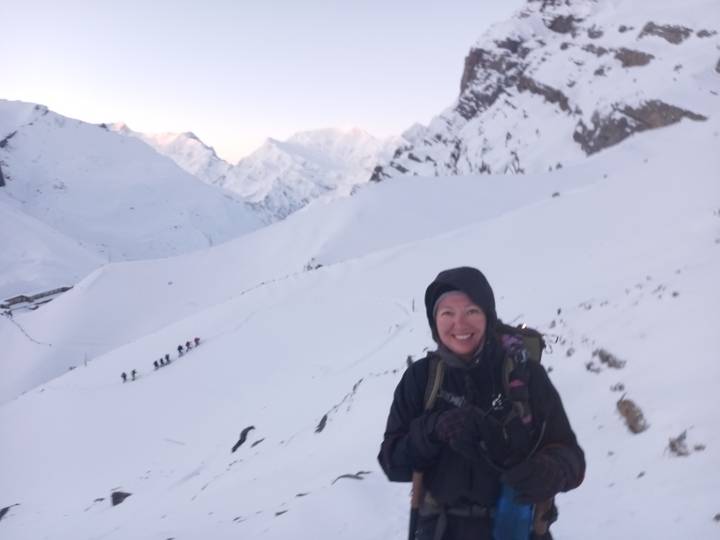 Smiling trekker in winter gear on snowy trail with line of hikers behind in soft dawn light.