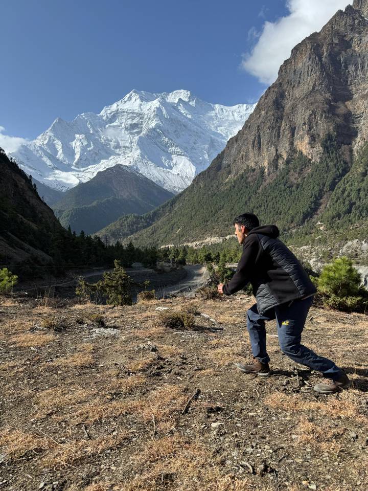 Trekker stretches arms while overlooking a forested Himalayan valley under clear sky.