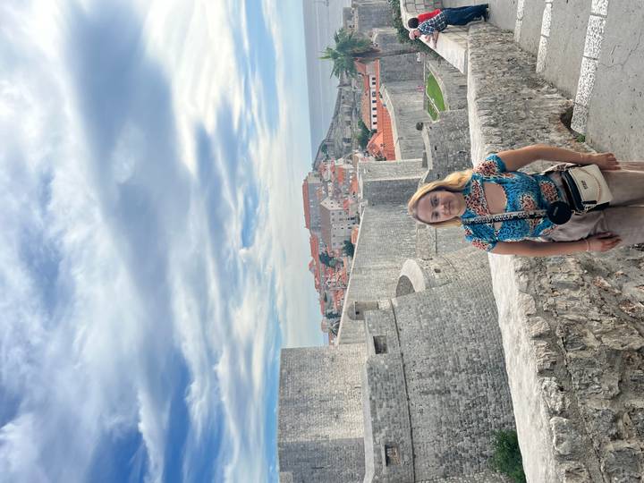 Traveler stands on Dubrovnik city walls with sweeping view of terracotta roofs and Adriatic Sea.