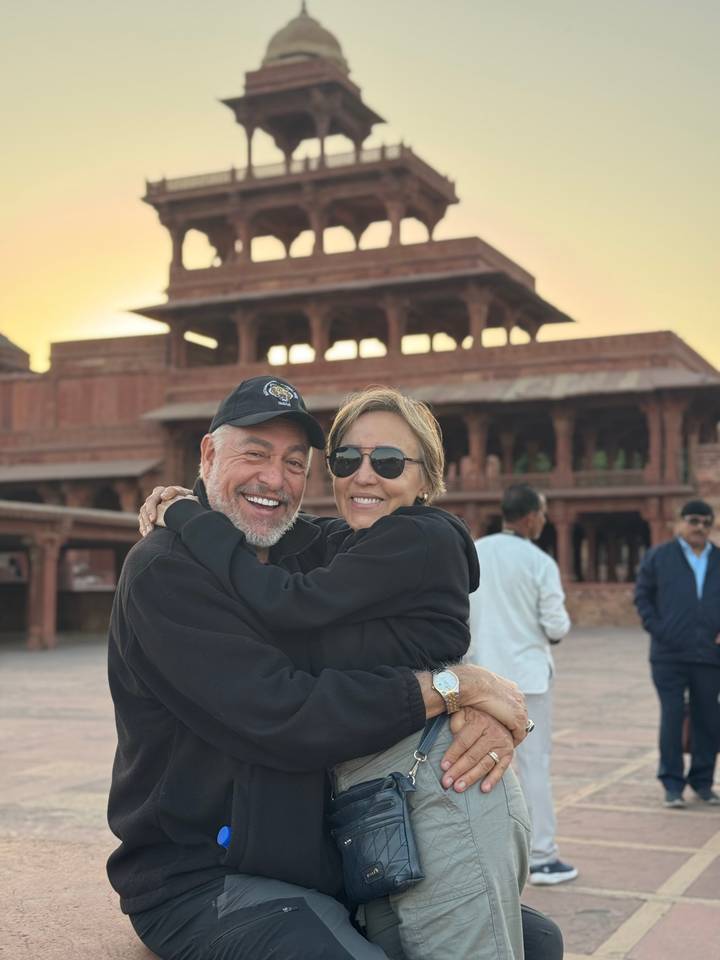 Smiling couple embrace in front of red sandstone palace at sunset glow in Fatehpur Sikri.