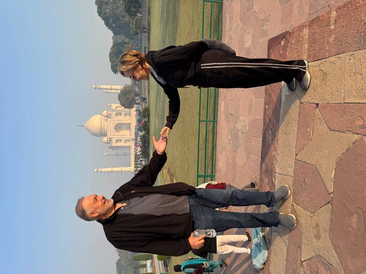 Playful perspective shot of couple with outstretched hands in front of distant Taj Mahal at dawn.