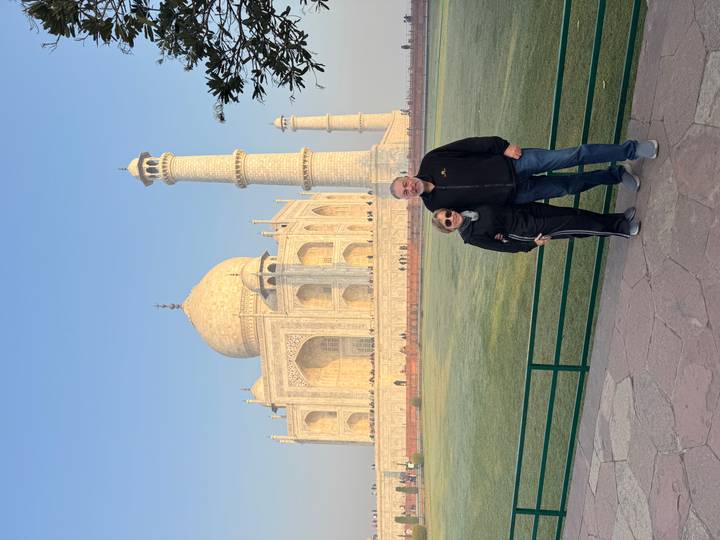 Couple stands arm in arm beside the Taj Mahal bathed in soft morning light.